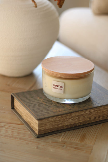Sences candle in Bonne nuit lavender scent with wooden lid on a book, surrounded by decorative items