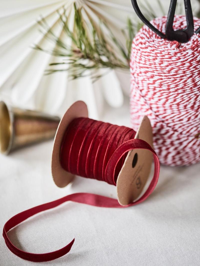 Spool of bordeaux red ribbon with a spool of red and white striped ribbon in the background.
