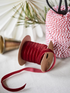 Spool of bordeaux red ribbon with a spool of red and white striped ribbon in the background.
