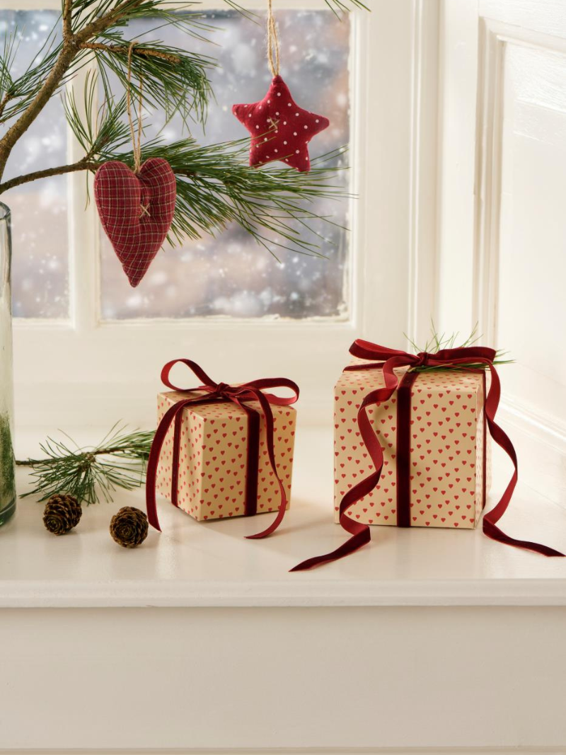 Two wrapped gifts with red ribbons on a windowsill with Christmas decorations.