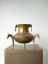 An antique-style bronze metal cauldron or pot with horse-shaped side handles, displayed on a square pedestal against a light gray background.