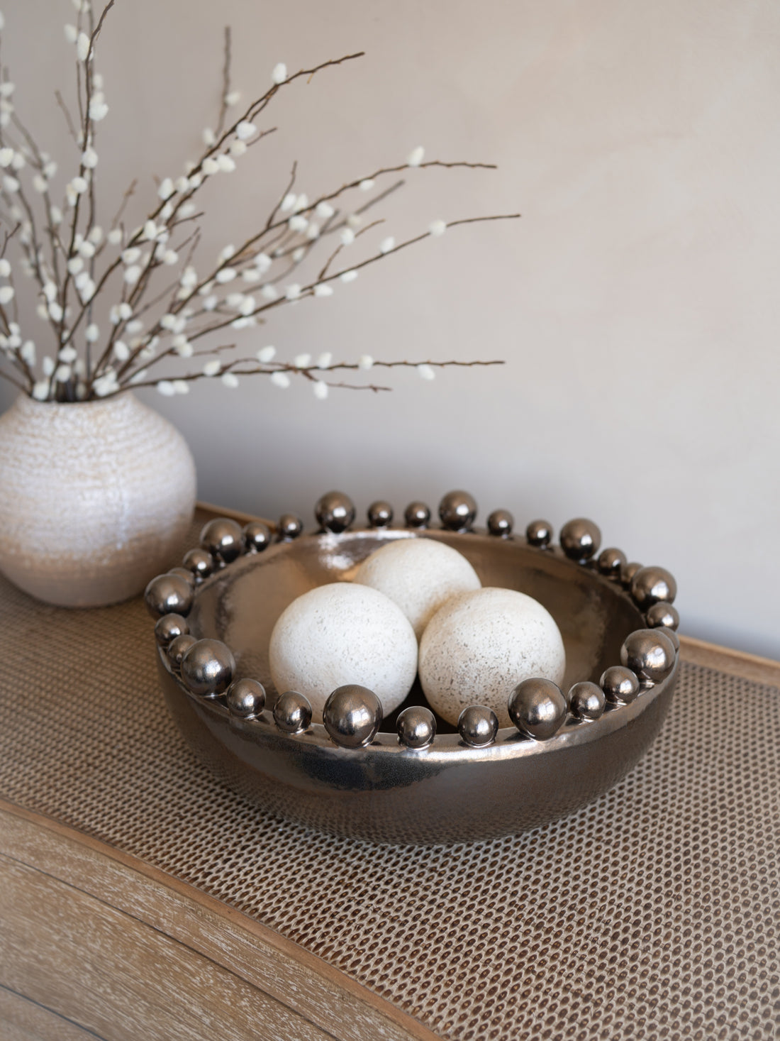 Decorative bowl with travertine balls and a vase with branches on a textured surface.