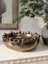 Decorative bronze metallic bowl with spherical embellishments on a surface with greenery in the background