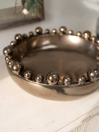 Bronze metallic bowl with spherical bobble embellishments on a white surface