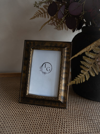 A rectangular picture frame with a distressed dark brown and gold patterned border, holding a white insert with a circular &