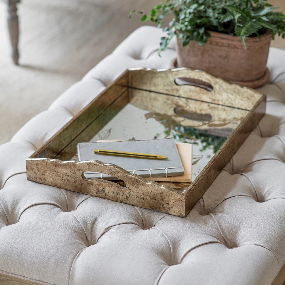 Wooden tray with stationery items on a tufted ottoman with a plant in the background