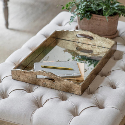 Wooden tray with stationery items on a tufted ottoman with a plant in the background