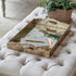 Wooden tray with stationery items on a tufted ottoman with a plant in the background