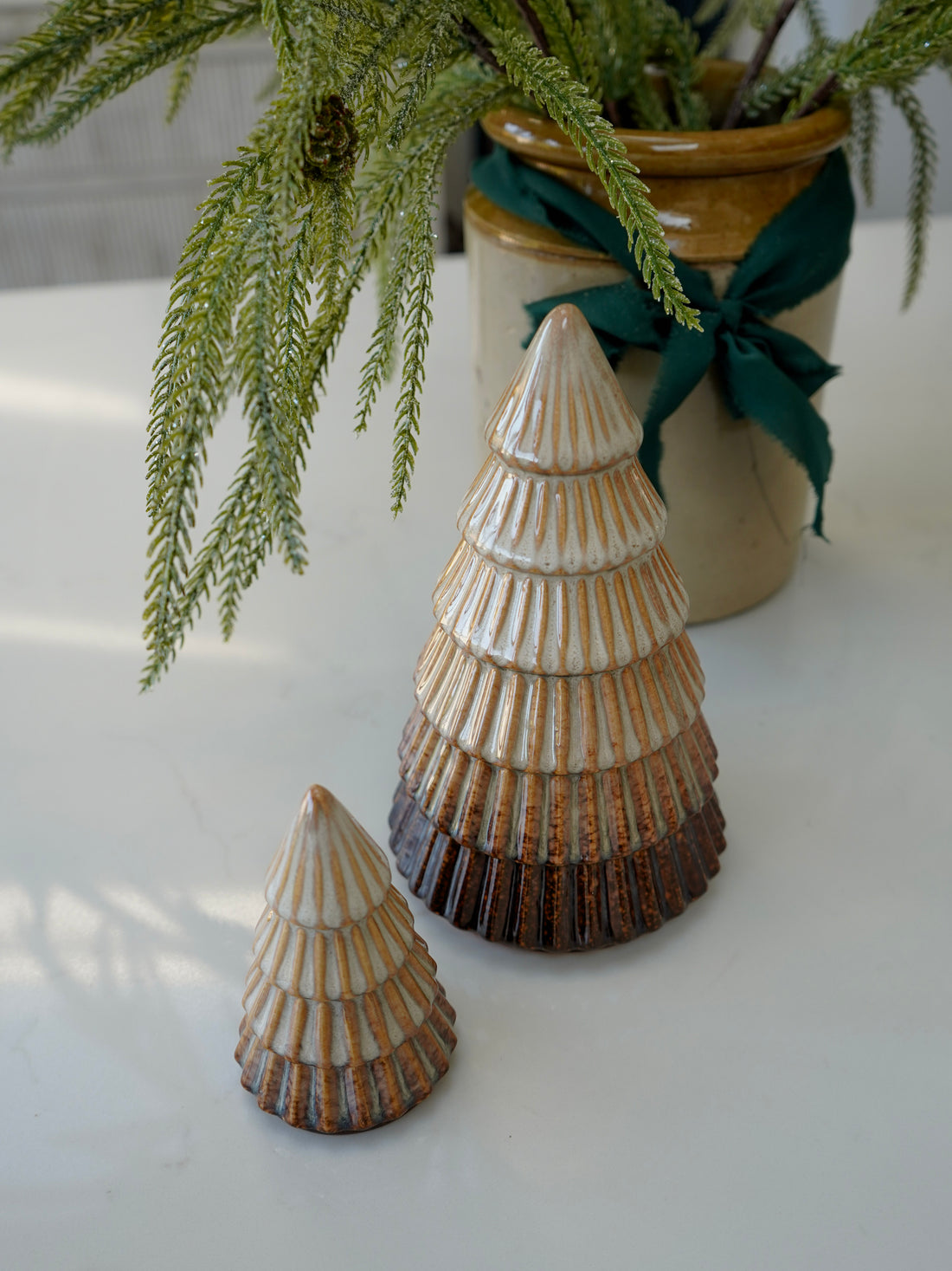 Two ceramic cone-shaped decorative items on a white surface with a plant in the background.