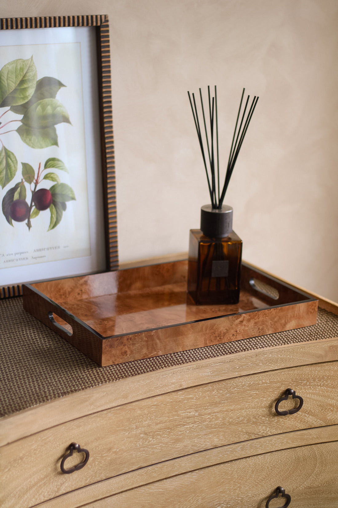 A diffuser bottle with reeds on a brown marbled effect tray next to a framed picture on a textured surface.