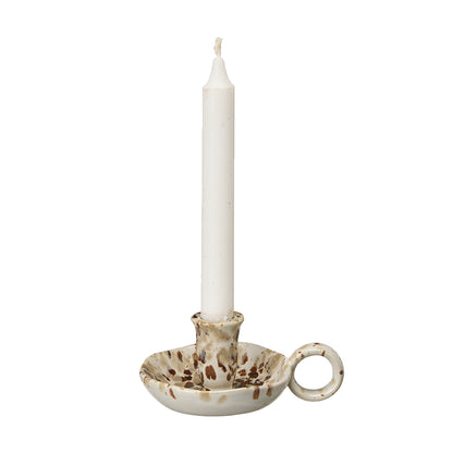 A white taper candle in a handmade ceramic candlestick holder with a brown speckled glaze and a side loop, shown on a plain white background.