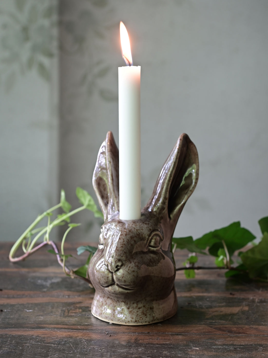 Ceramic rabbit-shaped candle holder with a lit candle on a wooden surface.
