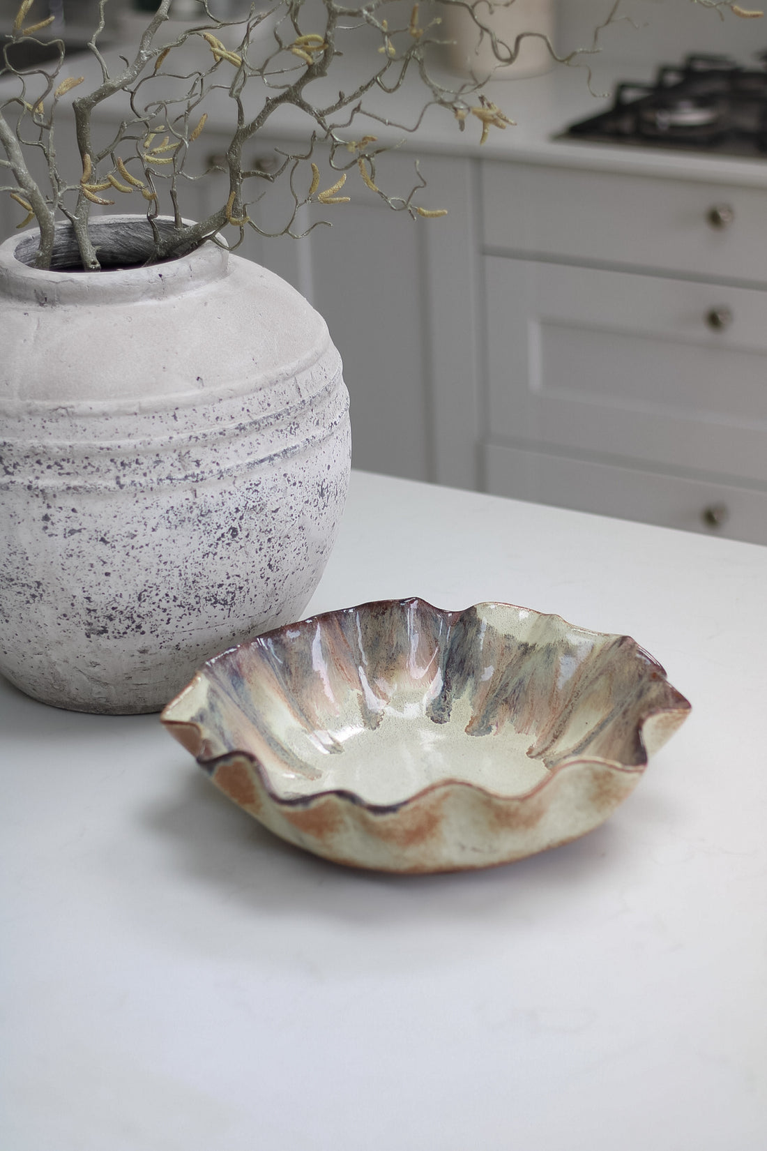 Ceramic pleated brown ombre bowl on a kitchen counter with a decorative plant and stove in the background