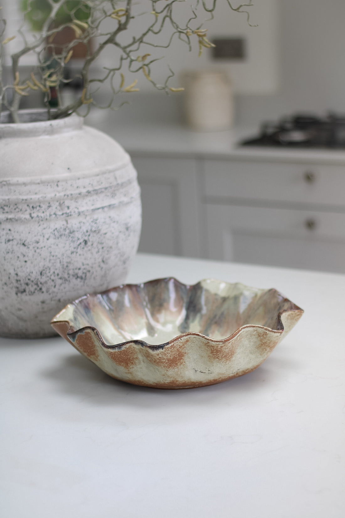 Ceramic brown ombre pleated bowl on a kitchen counter with a vase in the background