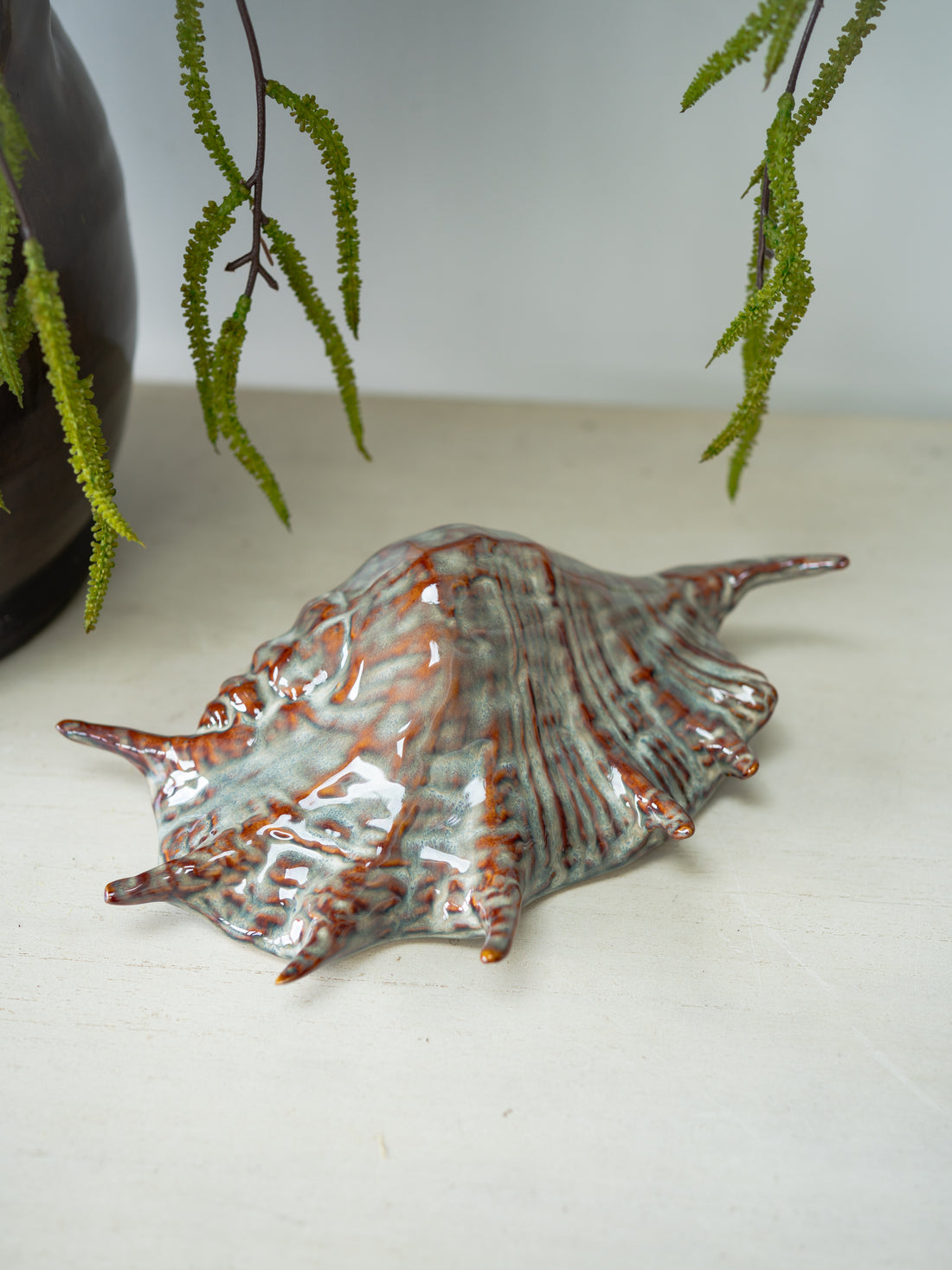 Decorative shell on a white surface with green leaves in the background