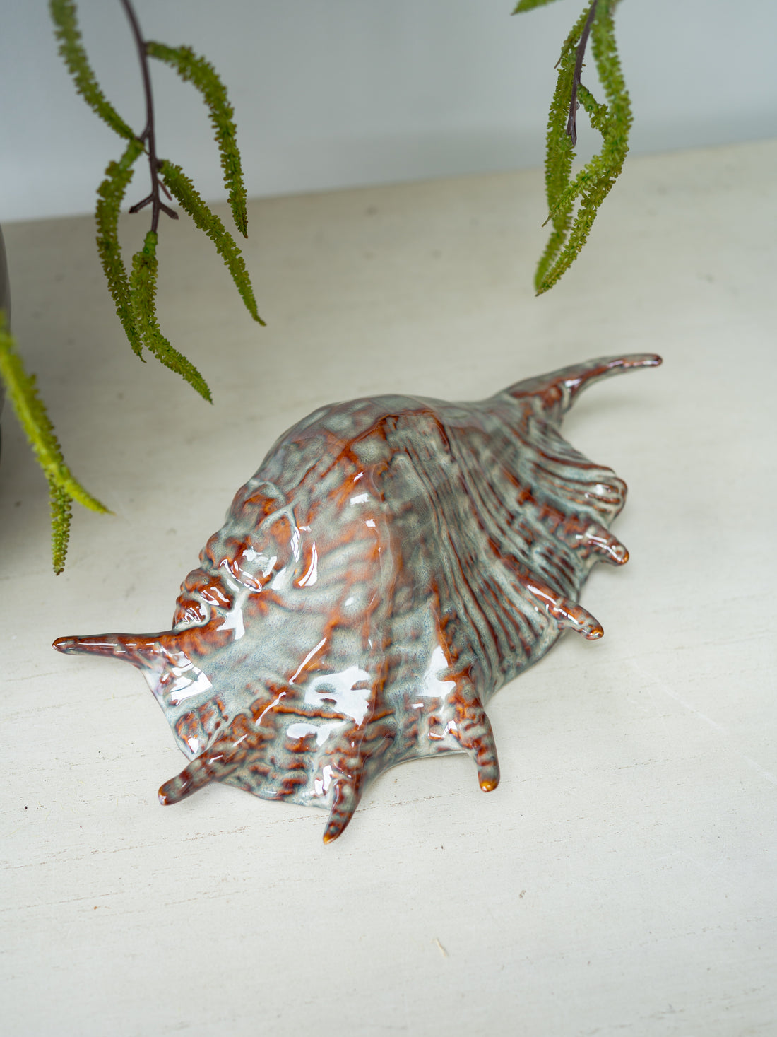 Decorative ceramic shell on a white surface with green leaves in the background