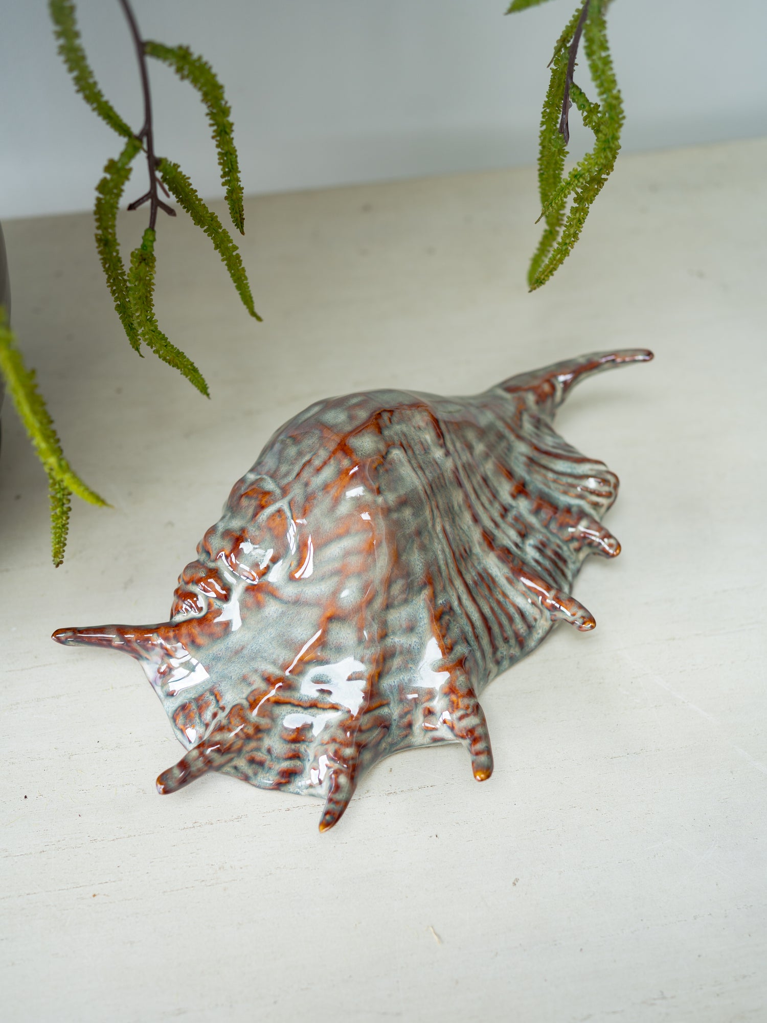 Decorative ceramic shell on a white surface with green leaves in the background