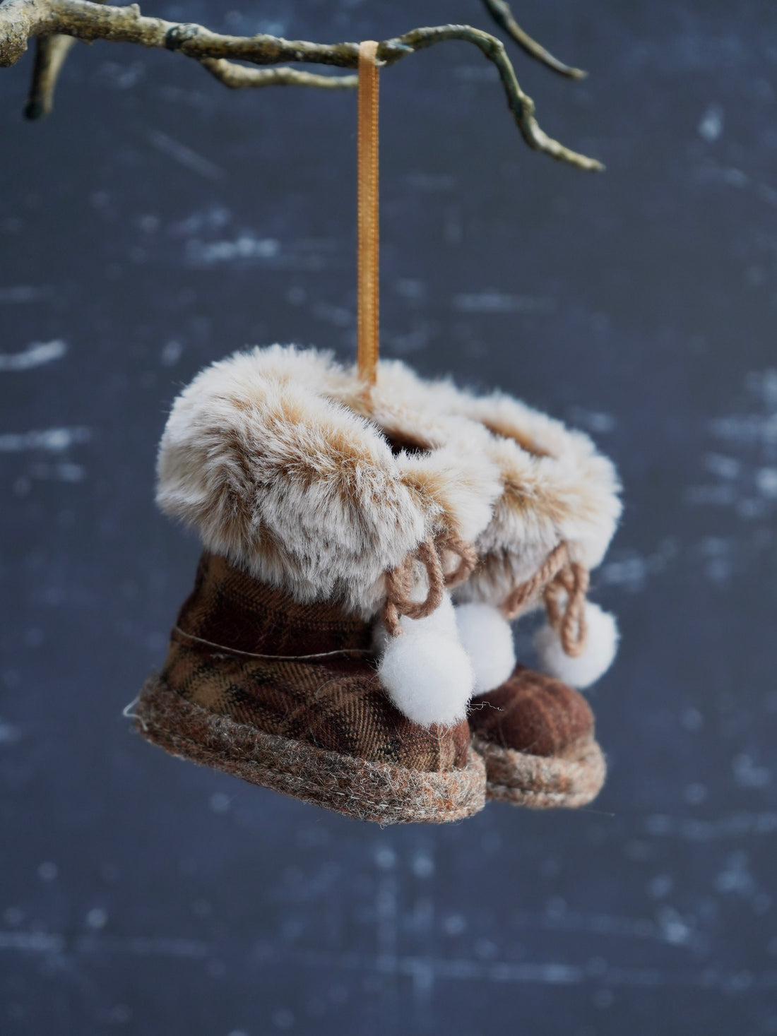 Decorative boots with fur and pom-poms hanging from a branch against a snowy background