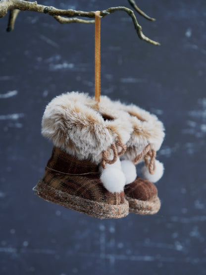 Decorative boots with fur and pom-poms hanging from a branch against a snowy background
