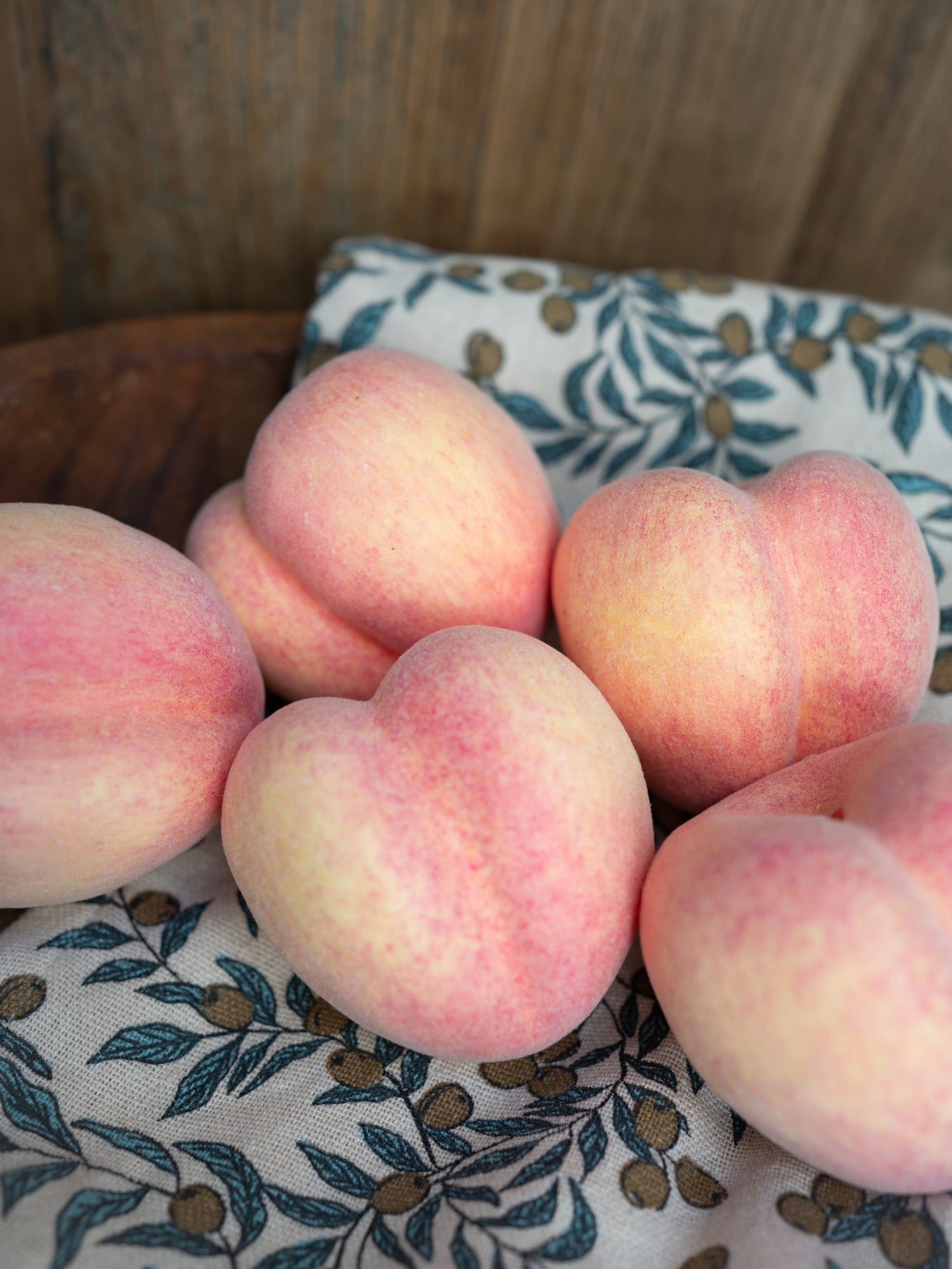 Group of faux decorative peaches on a patterned cloth with wooden background