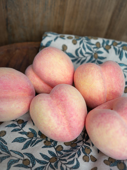 Group of faux decorative peaches on a patterned cloth with wooden background