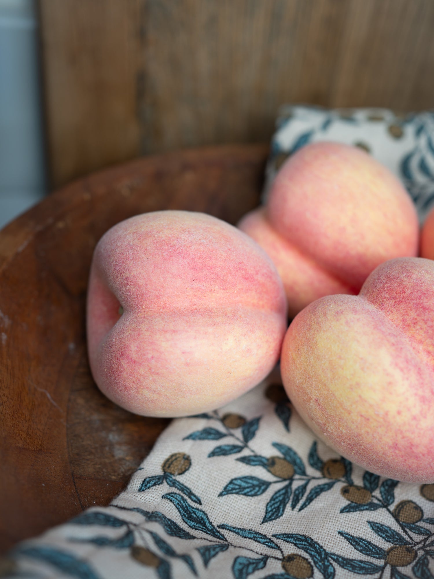 Faux peaches on a wooden surface with a patterned cloth underneath