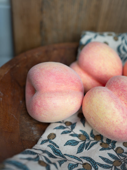 Faux peaches on a wooden surface with a patterned cloth underneath