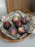 Decorative faux figs on a woven basket with a patterned cloth underneath