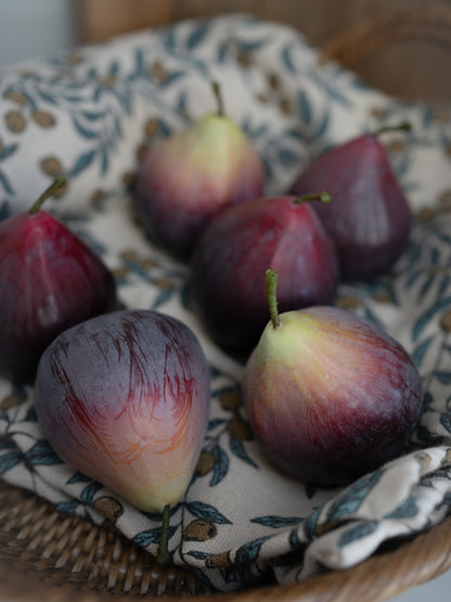 Decorative faux figs on a woven basket with a patterned cloth underneath