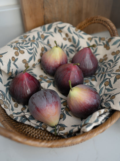 Decorative faux figs in a woven basket with a patterned cloth underneath