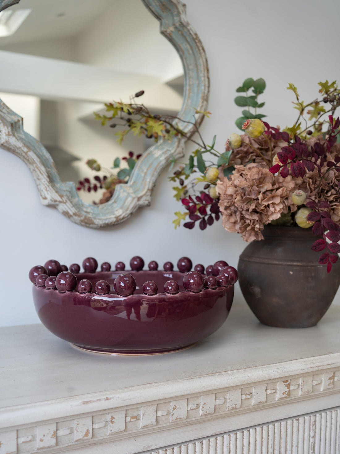 burgundy decorative bowl with spherical bobbles with autumn faux flower arrangement in the background