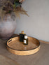Burl wood effect tray with perfume bottles on a textured surface, with a vase and plants in the background.