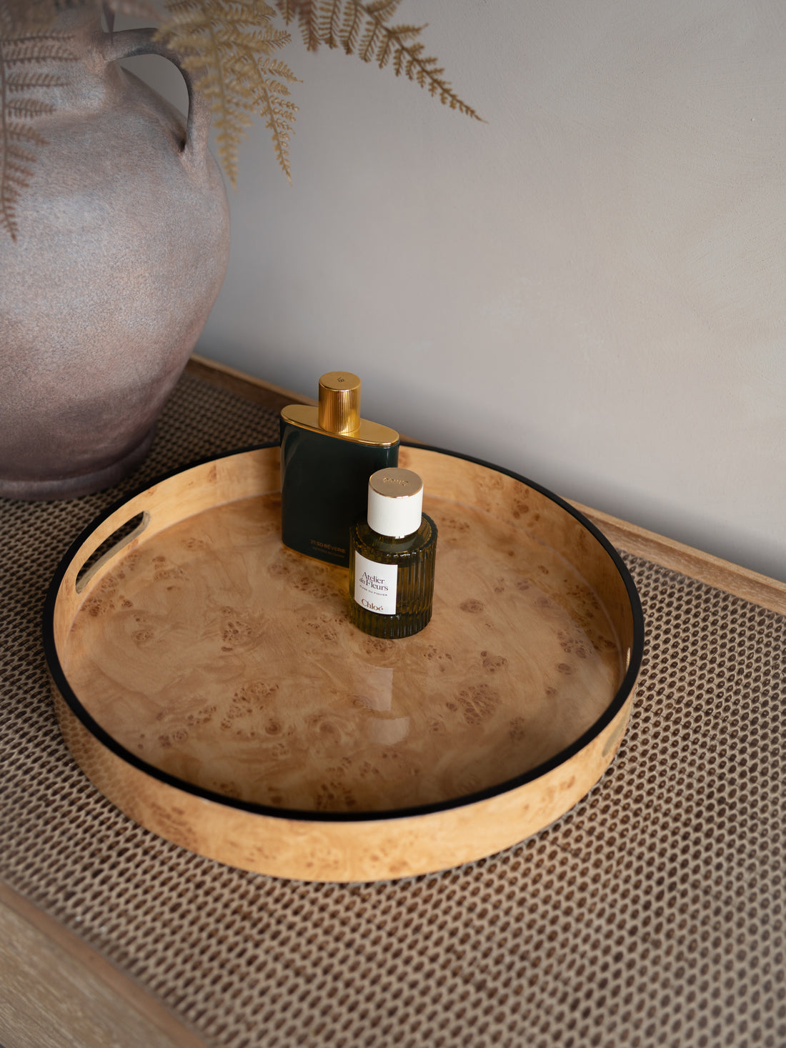 Round burl wood effect tray with black rim holding two bottles on a textured surface.