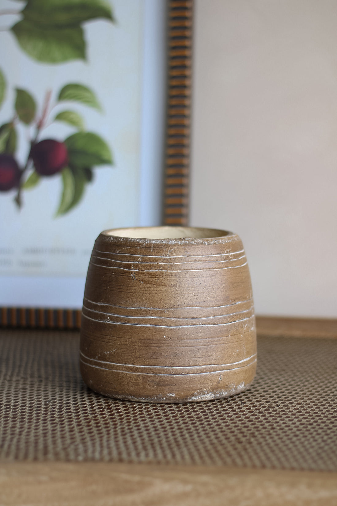 Brown ceramic pot on a textured surface with a framed picture in the background