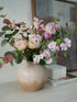 Vase with pink flowers on a surface with books and a framed picture in the background