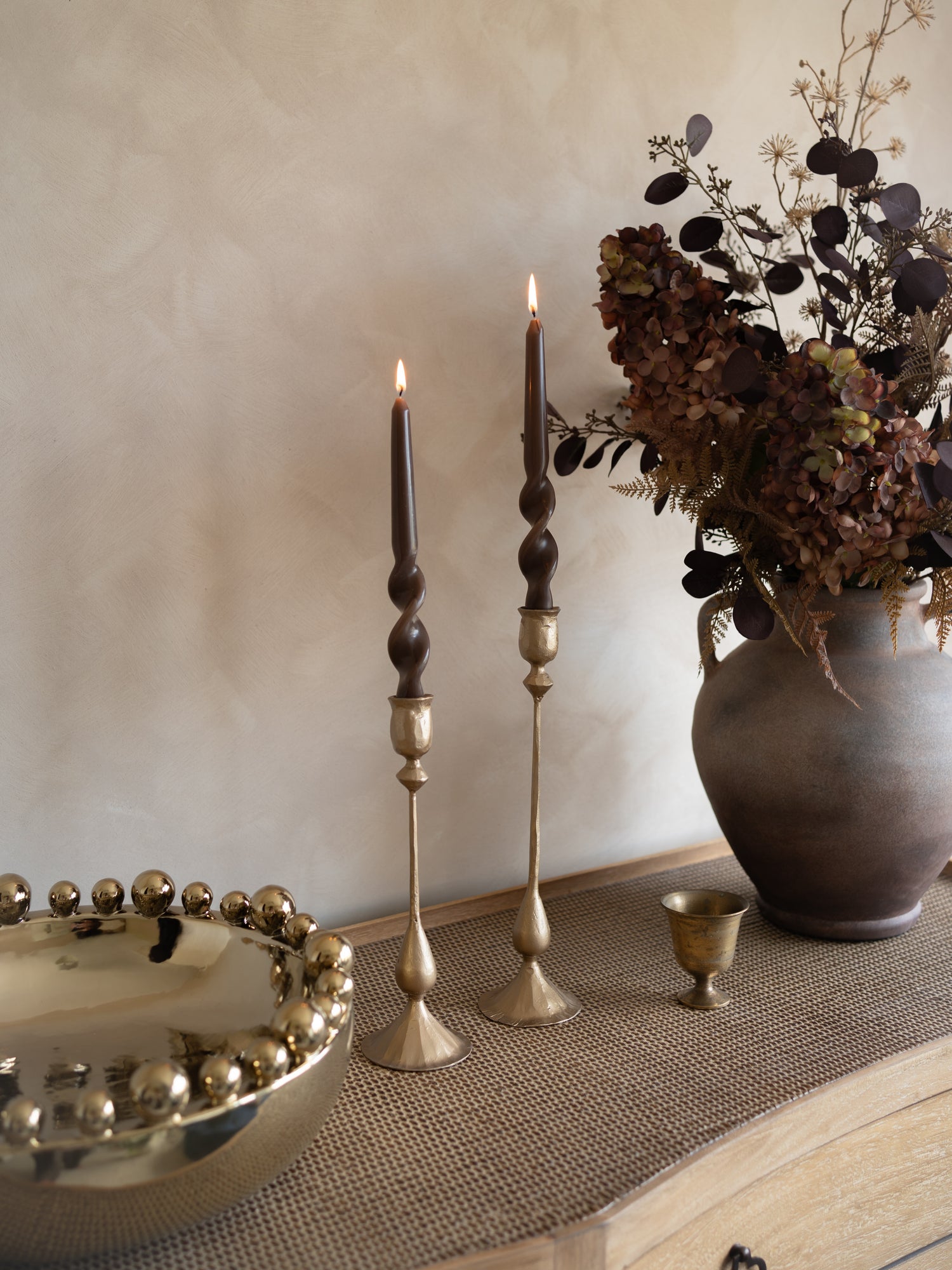 Decorative setting with candles, a vase, and a bowl on a textured surface.
