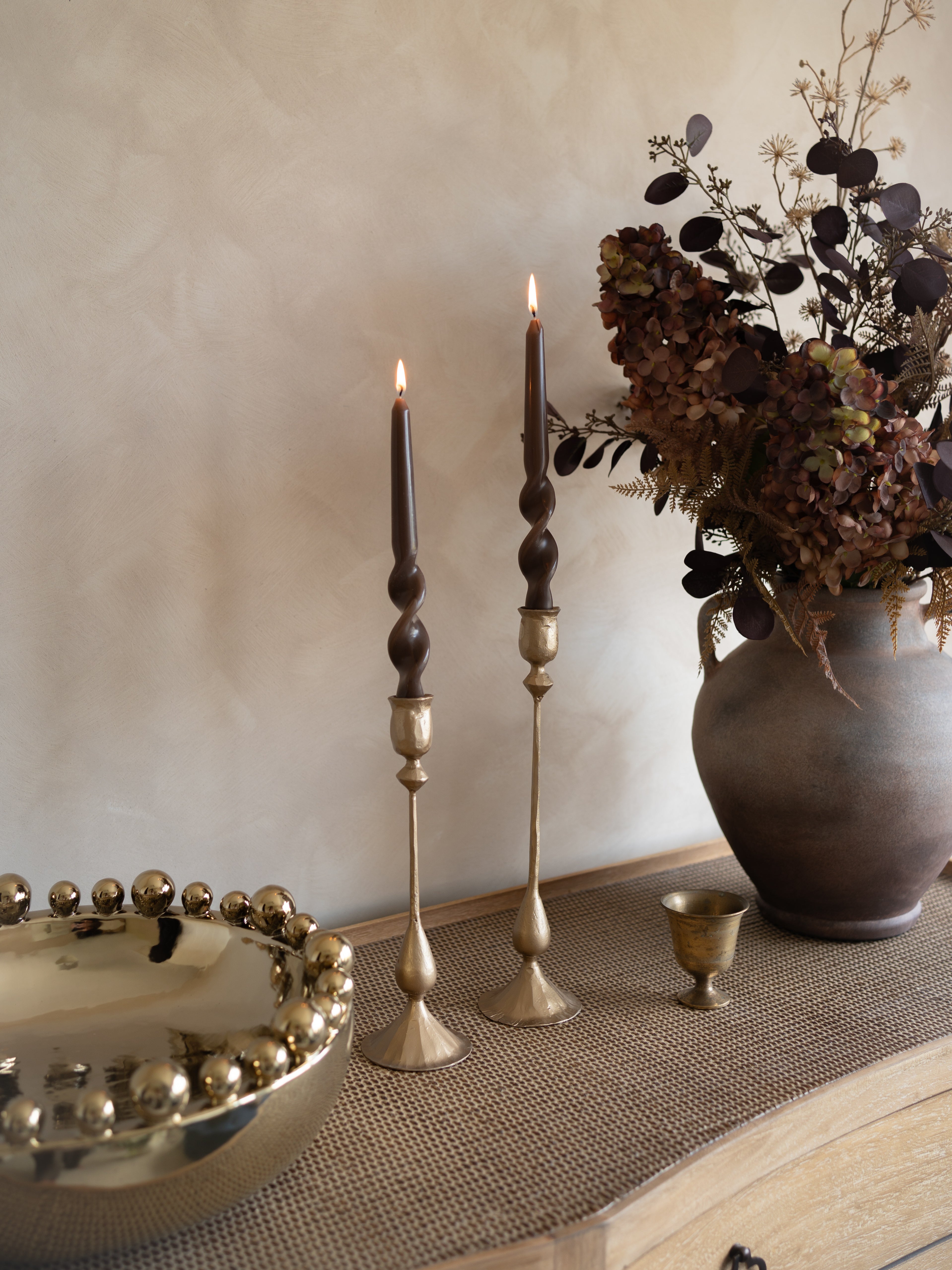 Decorative setting with candles, a vase, and a bowl on a textured surface.