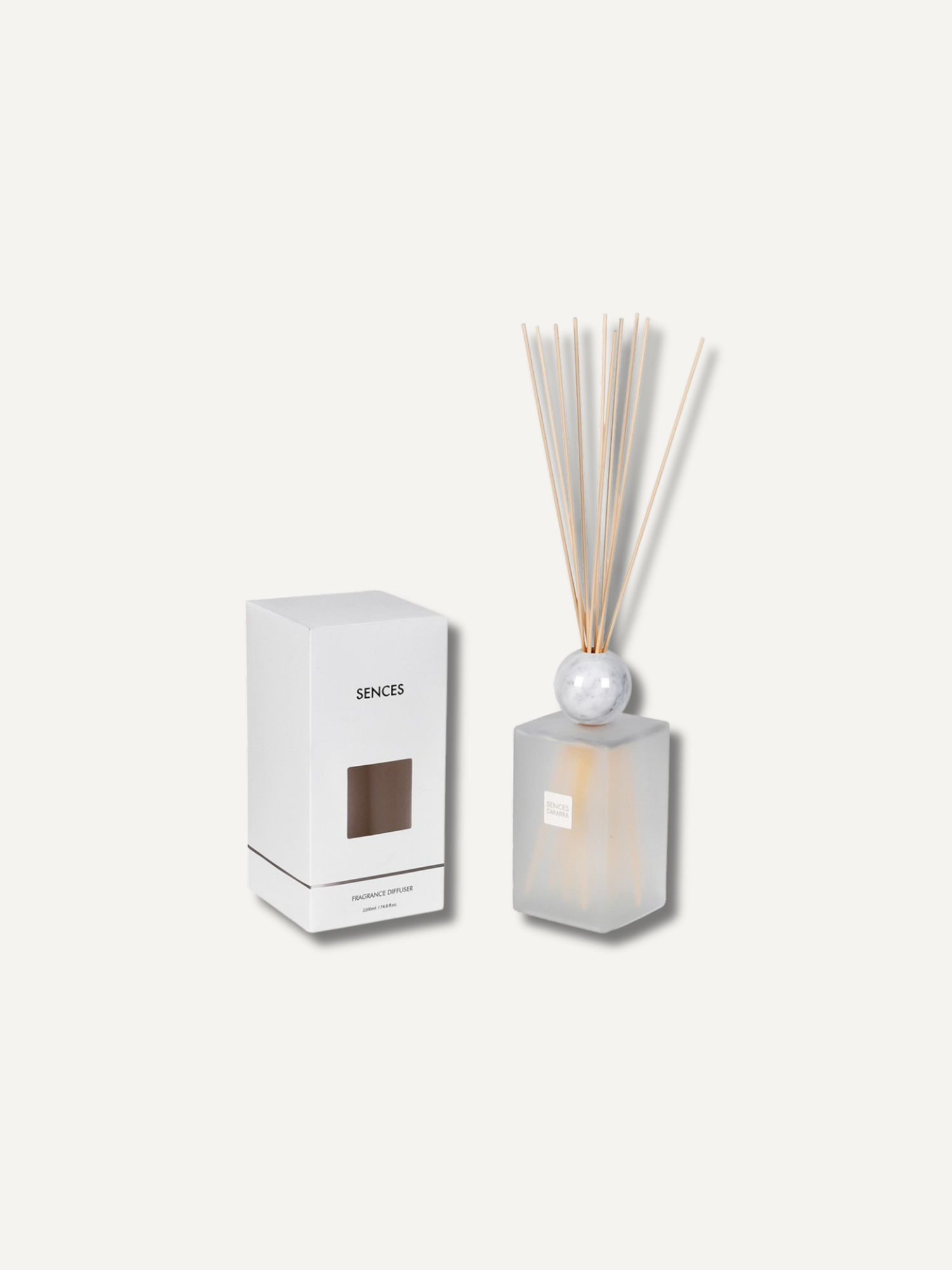 A reed diffuser set with a frosted glass bottle, white marble sphere, natural reeds, and its white packaging box on a light beige background.