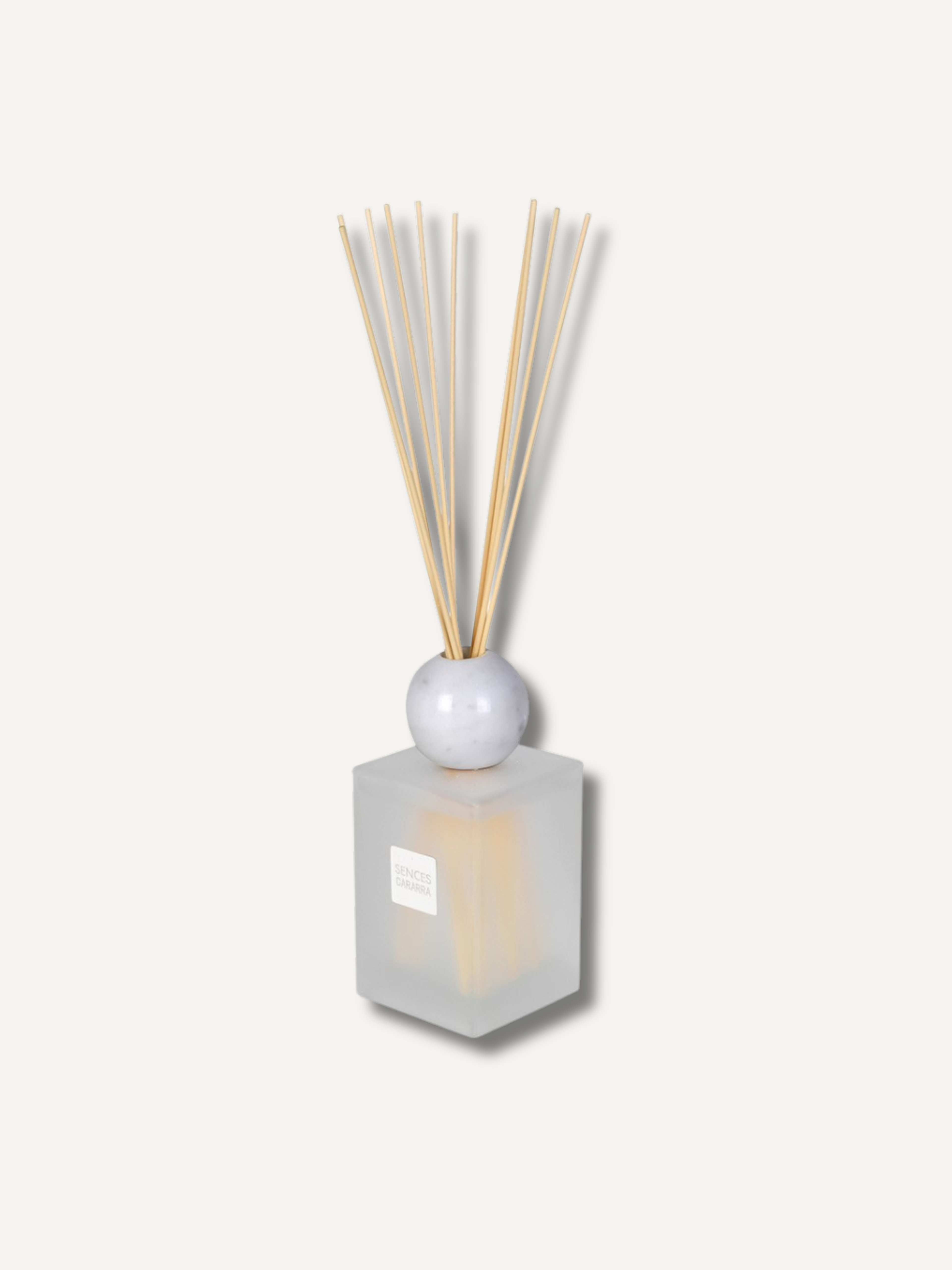 A reed diffuser with a frosted glass cube base, a white spherical stopper, and natural bamboo reeds, shown against a solid off-white background.