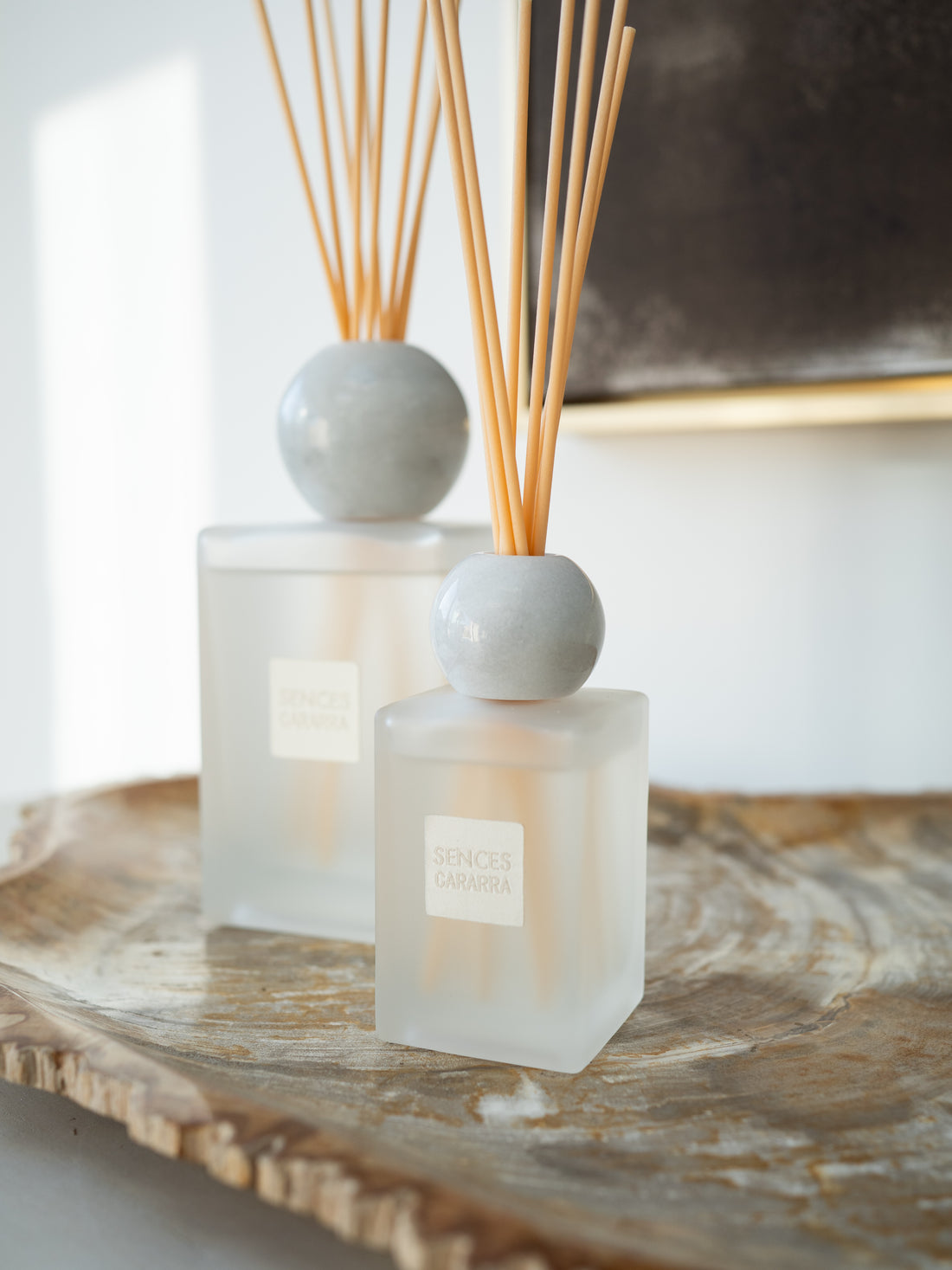 Two reed diffusers with frosted glass bottles, round white marble stoppers, and natural reed sticks, displayed on a rustic wooden tray.