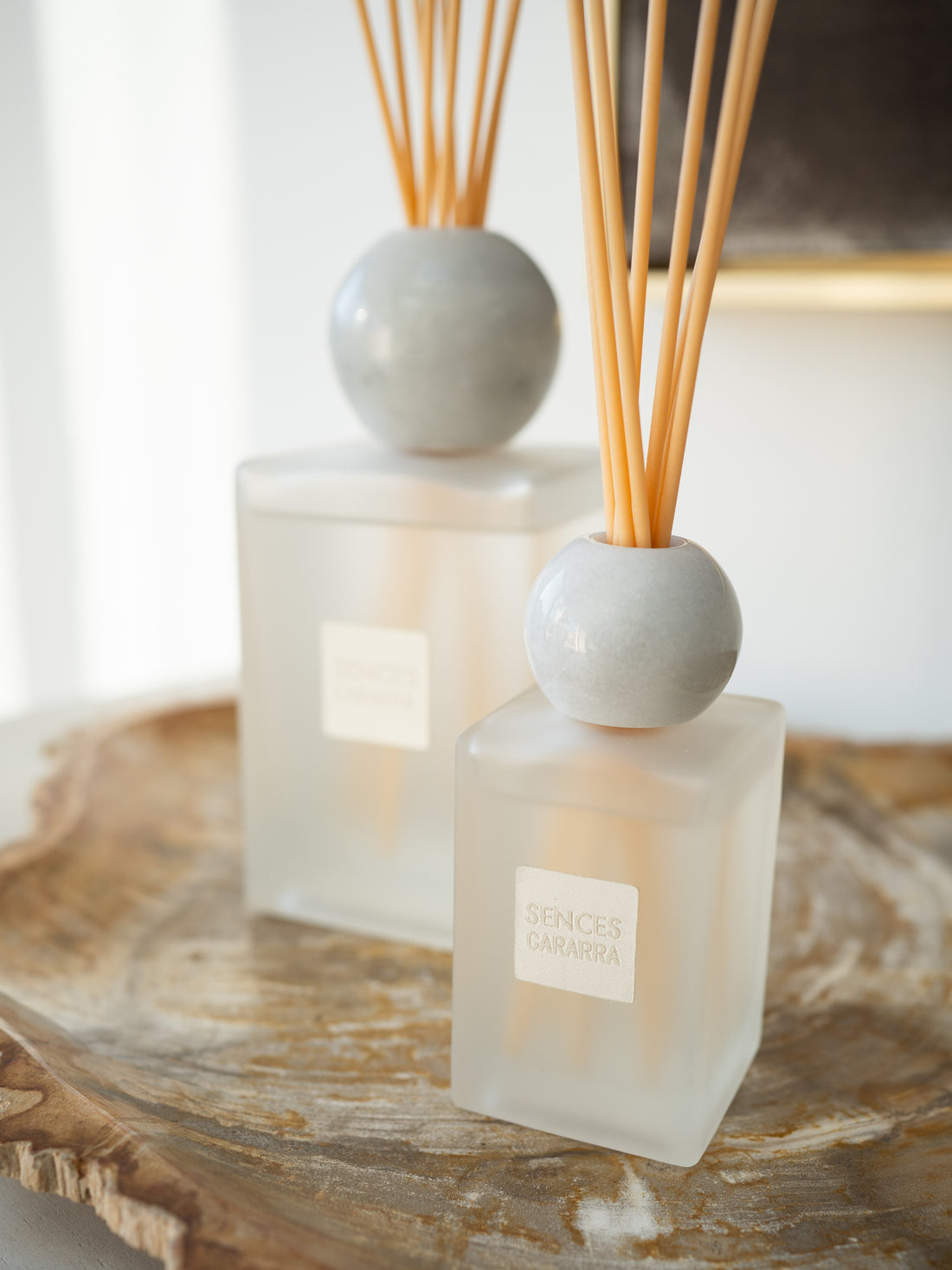 Two Sences reed diffusers with frosted glass bottles, round white marble tops, and natural wood reeds, displayed on a rustic wooden tray.