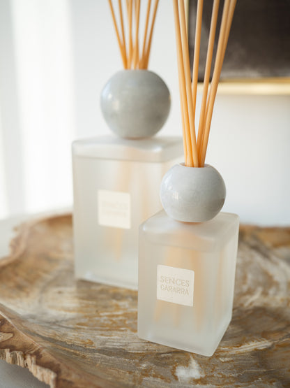 Two Sences reed diffusers with frosted glass bottles, round white marble tops, and natural wood reeds, displayed on a rustic wooden tray.