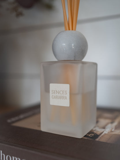 A frosted glass reed diffuser bottle with a white label reading &
