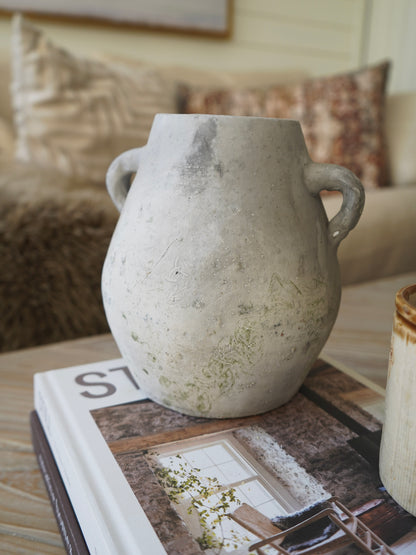 Decorative vase with handles on a table with books and a blurred background