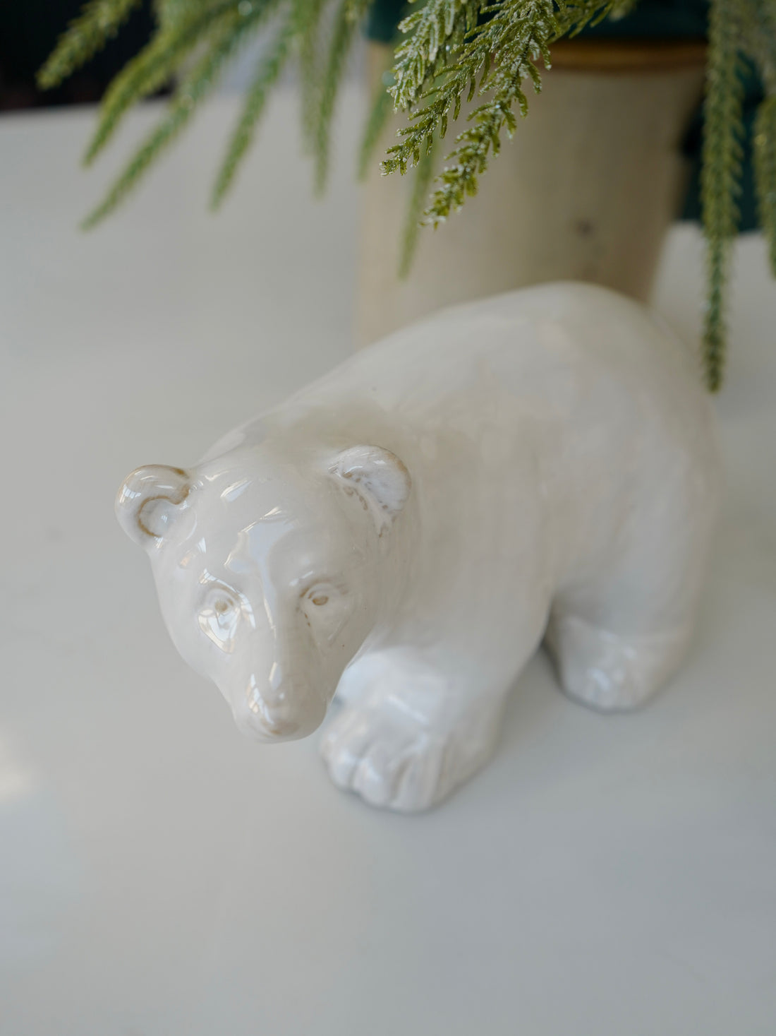 White ceramic bear figurine on a light surface with greenery in the background