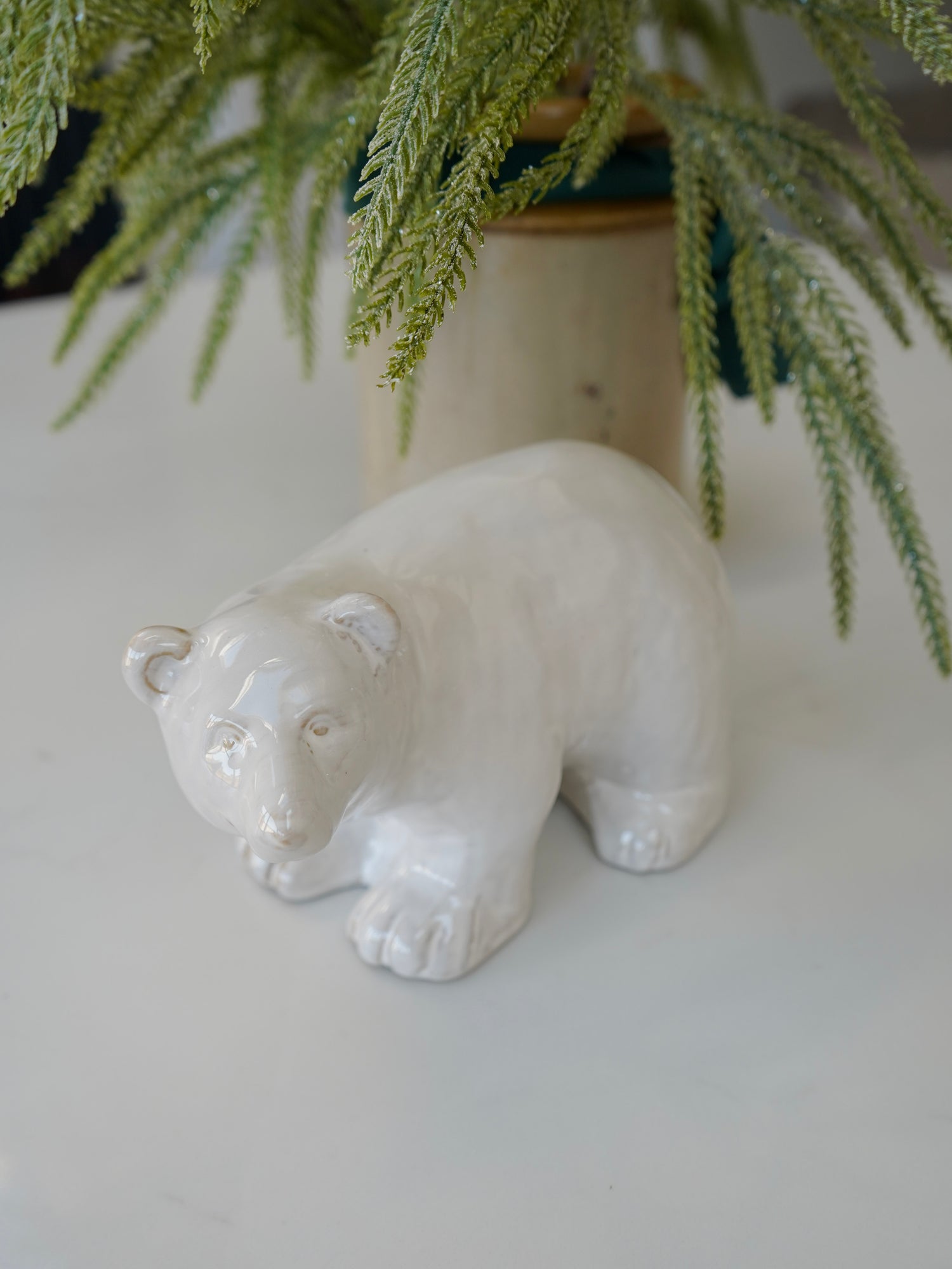 White ceramic bear figurine on a light surface with greenery in the background