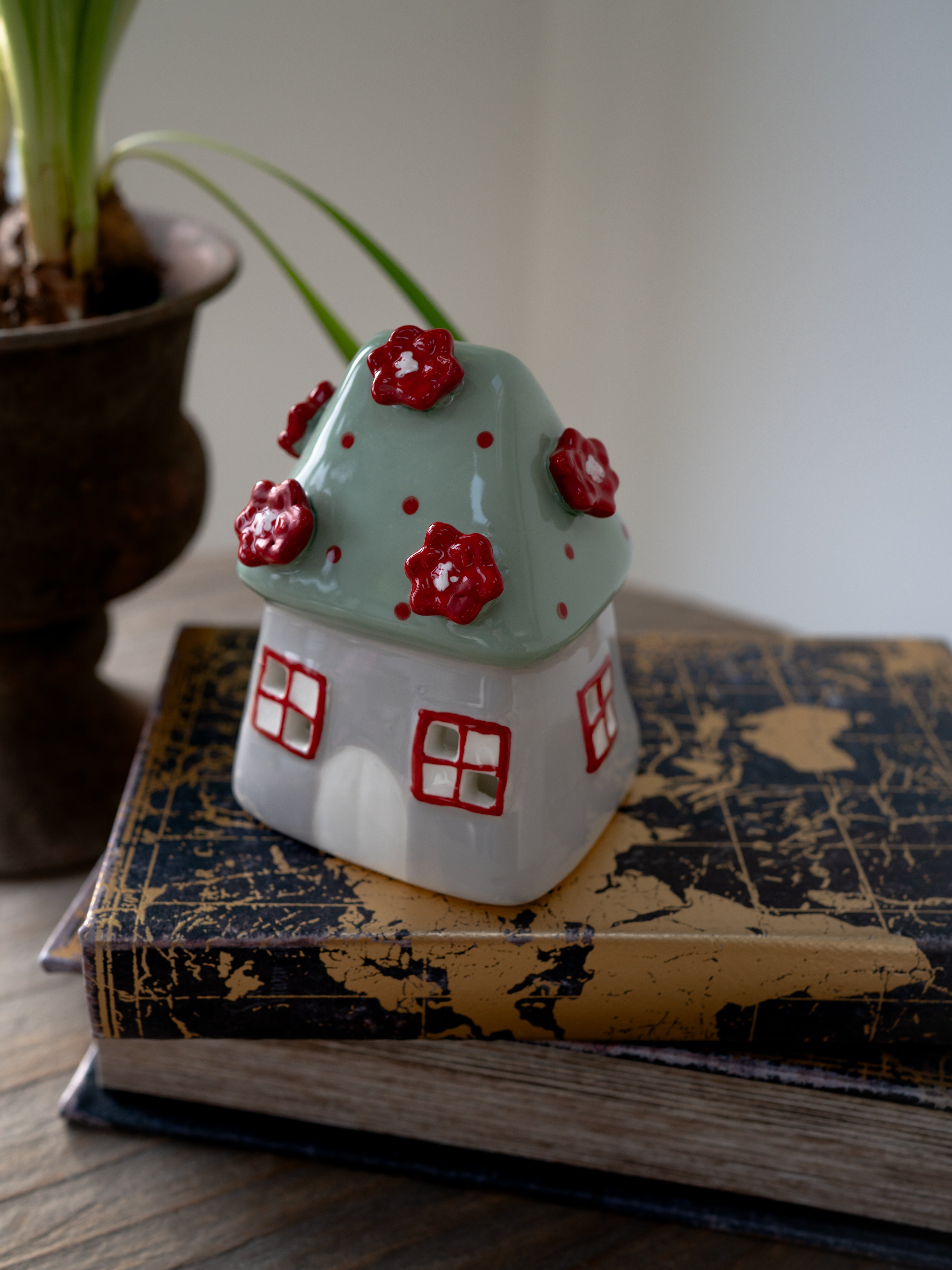 Ceramic house-shaped tea light holder with red flowers on top of a vintage book