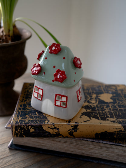 Ceramic house-shaped tea light holder with red flowers on top of a vintage book