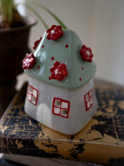 Ceramic house-shaped tea light holder with red floral designs on a textured surface