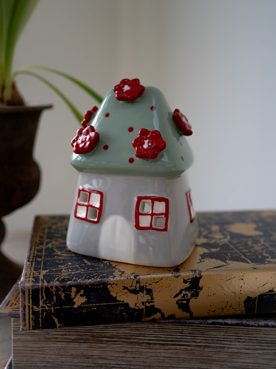 Ceramic house-shaped tea light holder with red flowers on a textured surface